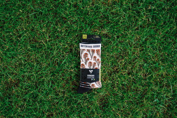 Packaged pair of Outeniqua Bound fynbos socks lying on green grass