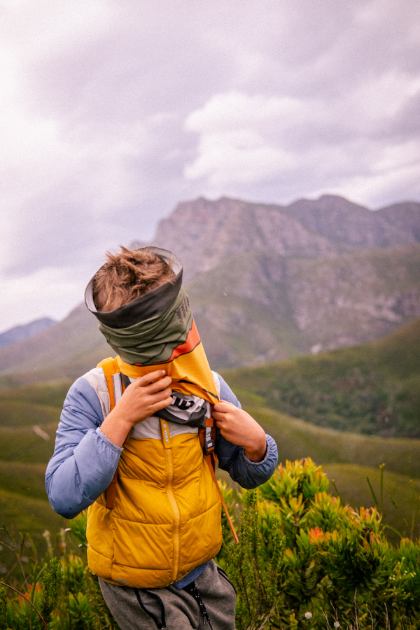 Child pulling a green buff over their face in front of mountains