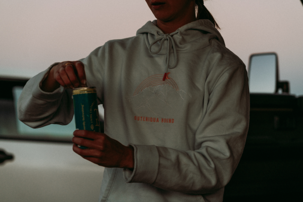 Woman in a cream Moonrise hoodie opening a drink can
