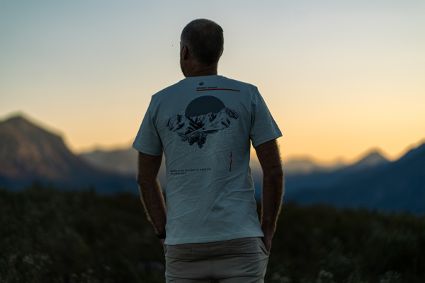 Man in a light blue Outeniqua Bound summit T-shirt facing mountains at sunset